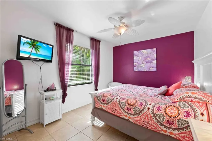 Bedroom featuring a vibrant accent wall, tile flooring, window with blinds, and ceiling fan