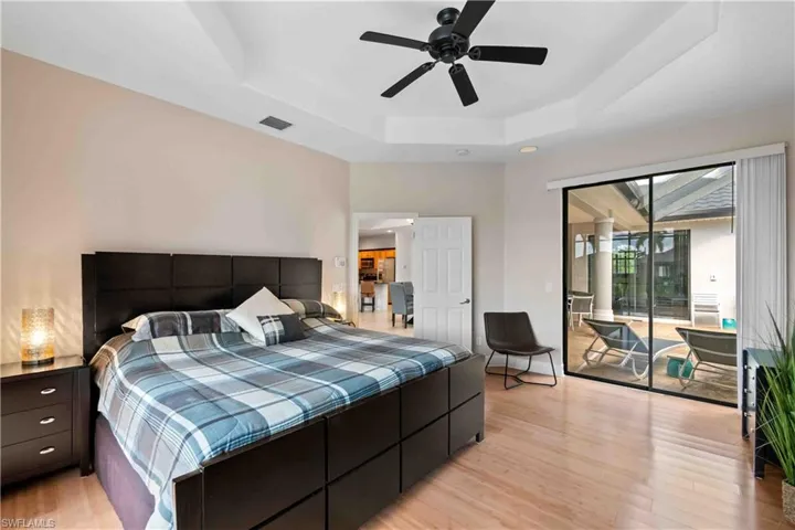 Bedroom with ceiling fan, access to exterior, a raised ceiling, and light wood-type flooring