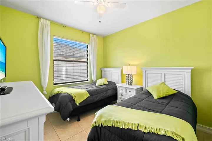 Bedroom featuring two white louvered headboards, a white bedside table, and a window with blinds