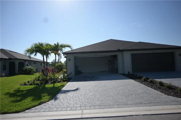View of front of home with decorative driveway, stucco siding, roof with shingles, and a front lawn