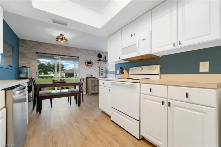 Kitchen with range, white cabinetry, dishwashing machine, light hardwood / wood-style floors, and a raised ceiling