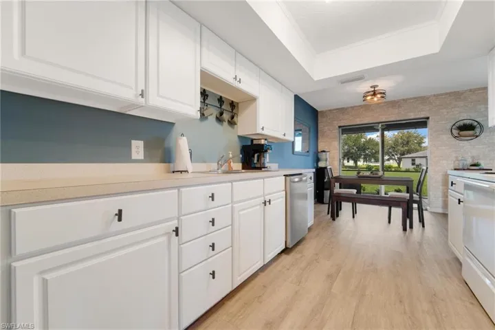 Kitchen featuring light hardwood / wood-style floors, white cabinetry, dishwasher, and a raised ceiling