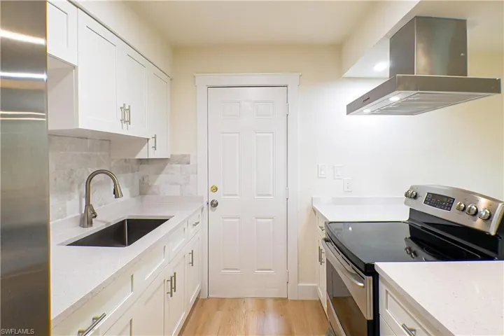 Kitchen featuring appliances with stainless steel finishes, light hardwood / wood-style flooring, sink, backsplash, and wall chimney exhaust hood