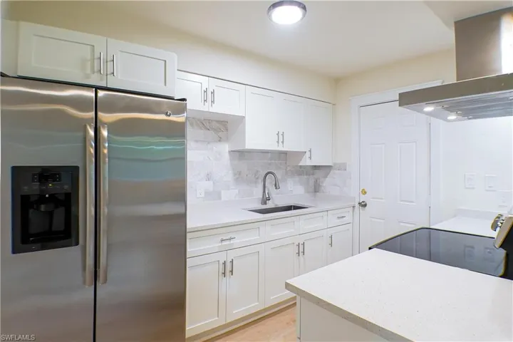 Kitchen featuring white cabinets, wall chimney exhaust hood, sink, stainless steel fridge, and backsplash