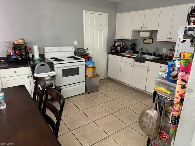 Kitchen with electric stove, light tile patterned flooring, sink, and white cabinetry