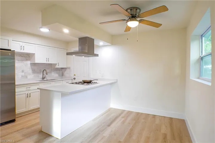 Kitchen with light hardwood / wood-style flooring, tasteful backsplash, stainless steel refrigerator, ceiling fan, and wall chimney exhaust hood
