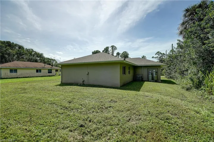 Rear view of property featuring a lawn and central AC unit