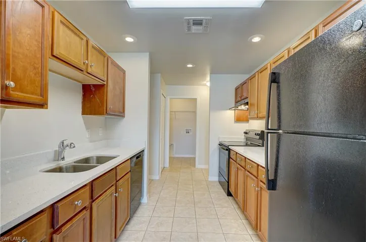 Kitchen featuring light stone counters, light tile patterned floors, sink, and black appliances
