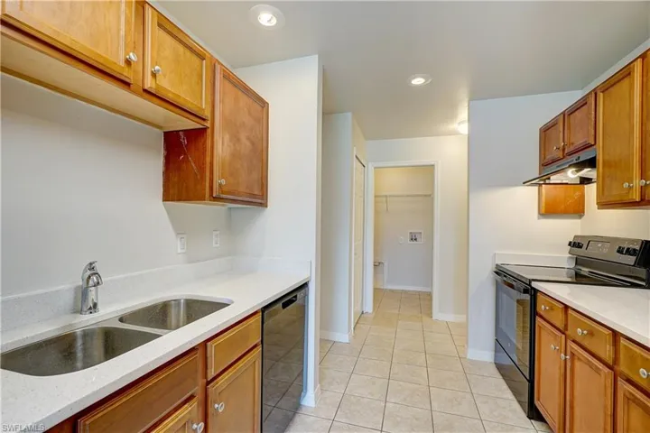 Kitchen with light tile patterned floors, light stone countertops, sink, and black appliances