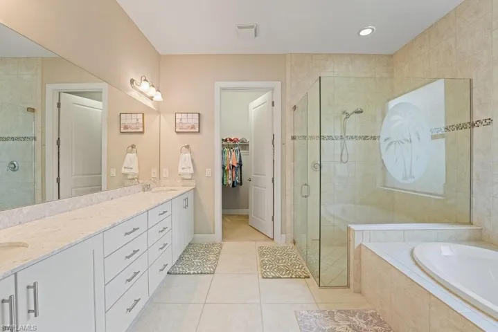 Dual vanity with stone countertop, large mirror, glass-enclosed shower, soaking tub, and tiled flooring