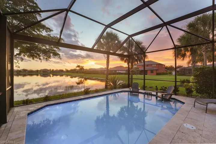 Screened lanai with heated saltwater pool featuring travertine decking, panoramic water views, and abundant natural light through geometric glass ceiling panels