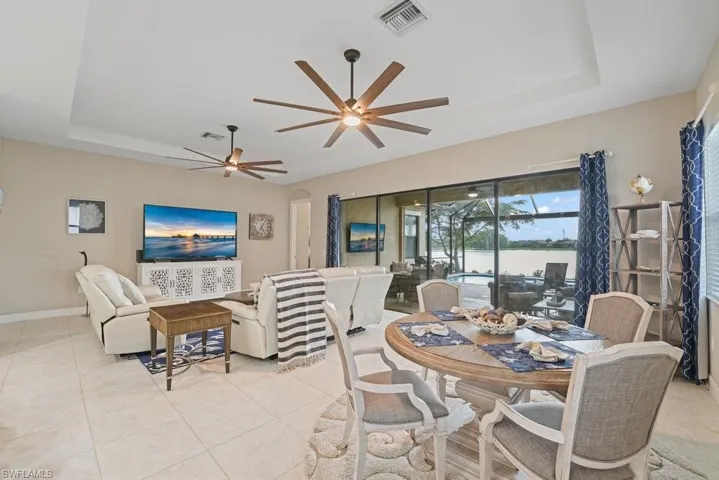 Open-concept living area with tray ceiling, tile flooring, and direct access to an outdoor screened patio