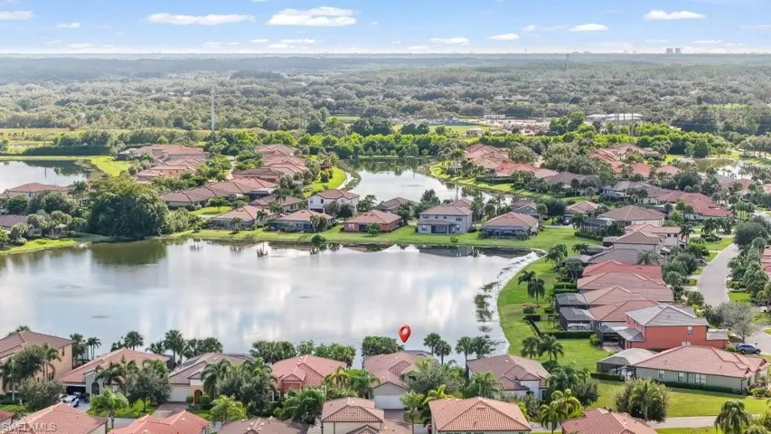 Aerial perspective showcasing residential properties with terracotta-style roofs, surrounded by a natural body of water, and bordered by extensive natural landscaping