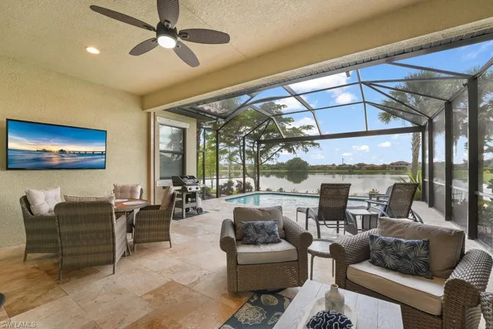 Screened-in lanai with a ceiling fan and recessed lighting, featuring stone tile flooring, an outdoor television mount, and a built-in pool