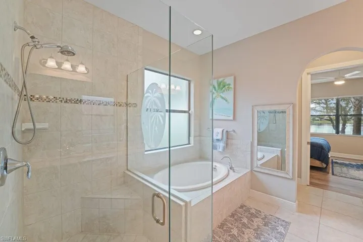Glass-enclosed shower with a built-in bench, a separate soaking tub, and tiled walls with a decorative accent band