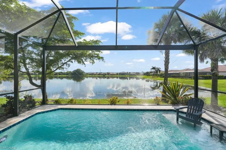Screened-in outdoor pool featuring a water outlook, surrounding green landscaping, and mature palm trees