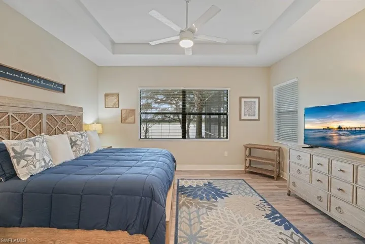 Tray ceiling with a ceiling fan, wood-finish flooring, and window blinds