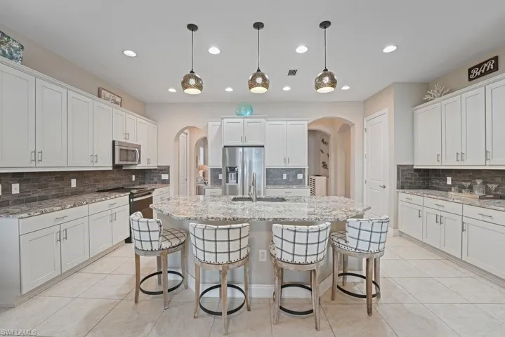 Expansive kitchen featuring white cabinetry, granite countertops, stainless steel appliances, and a tiled backsplash