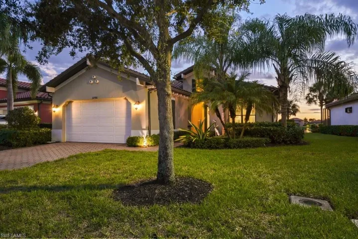Stucco exterior with a tiled roof, paver driveway, lush landscaping, and integrated exterior lighting