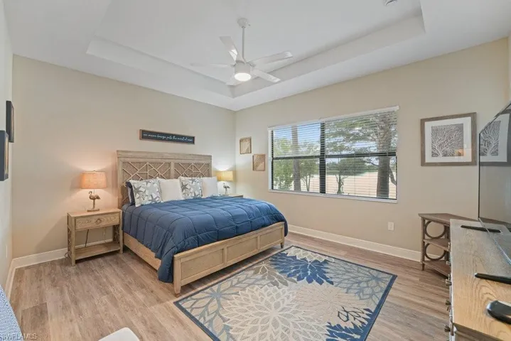 Tray ceiling with a ceiling fan, wood-finish flooring, and a large window with blinds