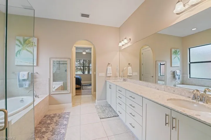 Dual vanity with integrated sinks and a continuous countertop, a built-in jetted tub, and a separate glass-enclosed shower