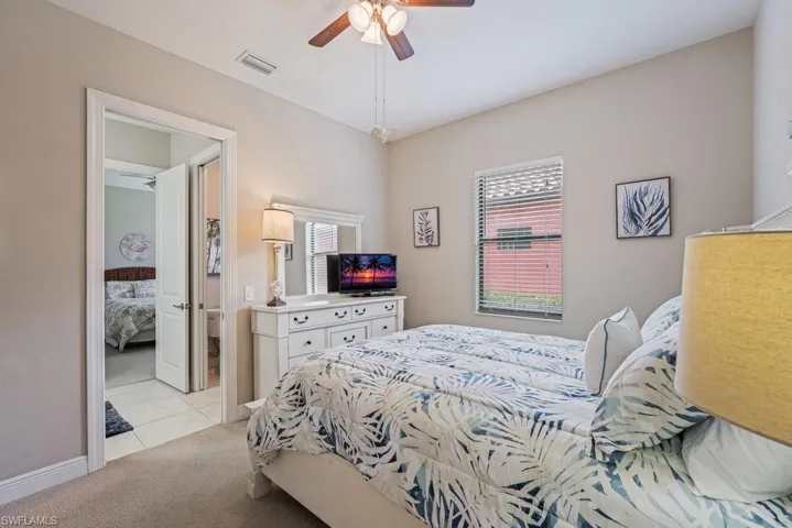 Neutral tone painted walls, ceiling fan with integrated lighting, window with horizontal blinds, carpeted flooring, and a doorway to an adjacent room