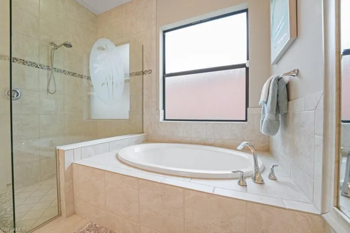 Integrated soaking tub with deck-mounted polished chrome fixtures, tile surround, and an adjacent tiled shower with a glass enclosure and decorative tile accent band