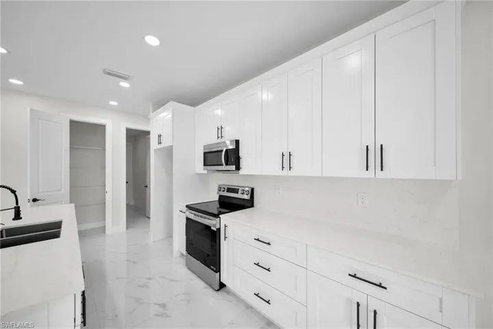 Kitchen featuring appliances with stainless steel finishes, white cabinetry, sink, and light stone countertops