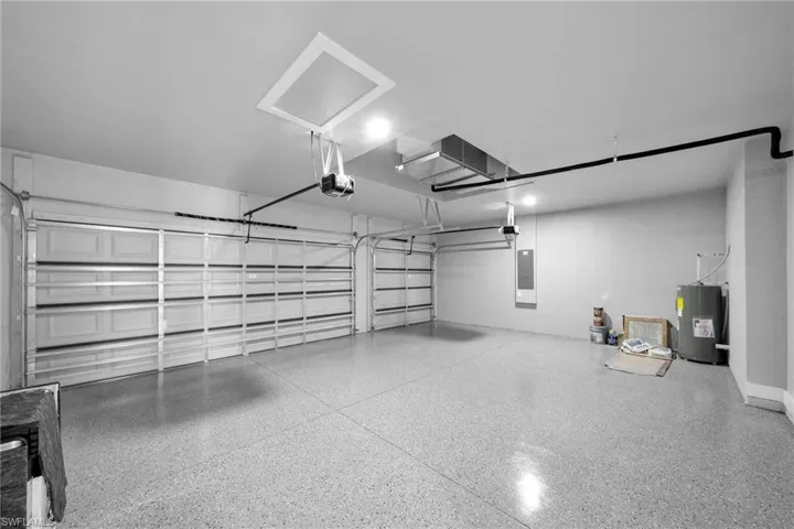 Garage with a garage door opener, electric panel, and electric water heater