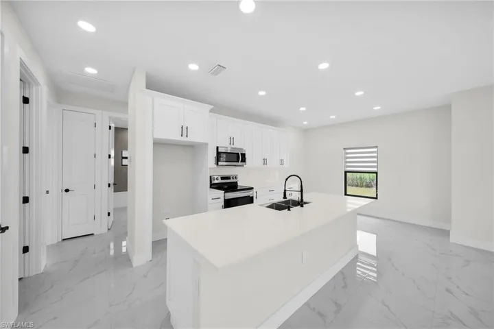 Kitchen featuring a kitchen island with sink, appliances with stainless steel finishes, white cabinetry, and sink
