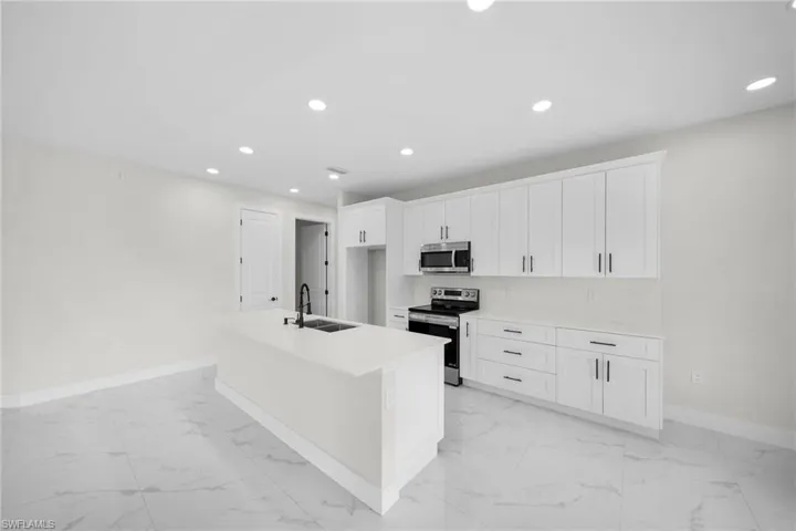 Kitchen featuring a center island with sink, appliances with stainless steel finishes, sink, decorative backsplash, and white cabinetry