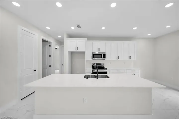 Kitchen with light stone counters, sink, appliances with stainless steel finishes, a center island with sink, and white cabinets