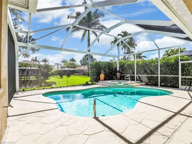 View of pool featuring a patio area, a yard, a pool with connected hot tub, and glass enclosure
