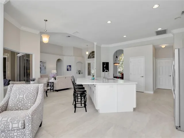 Kitchen with open floor plan, arched walkways, freestanding refrigerator, ornamental molding, and light countertops