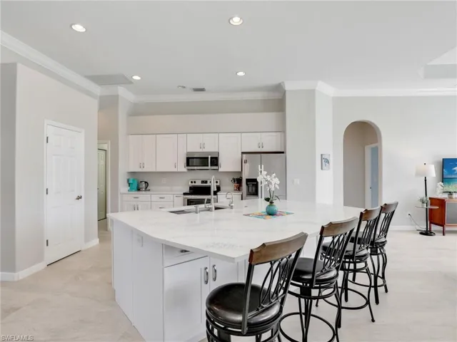 Kitchen featuring stainless steel appliances, ornamental molding, arched walkways, white cabinetry, and a large island