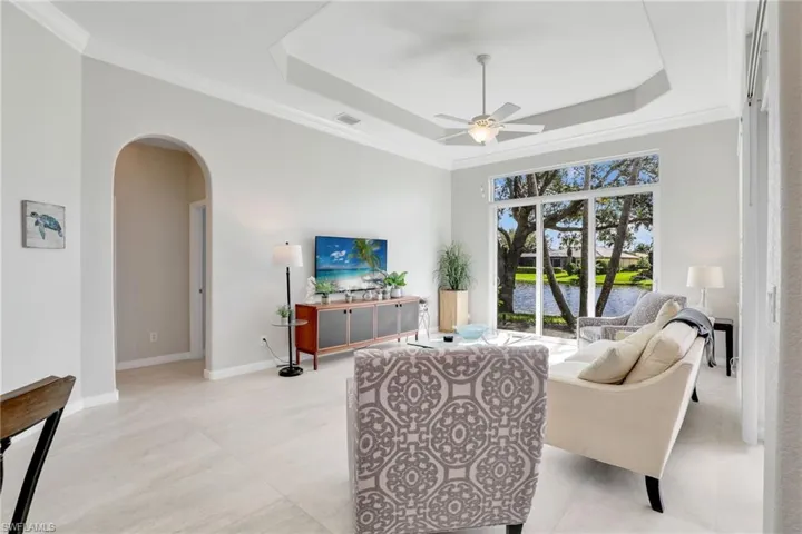 Living area featuring arched walkways, ceiling fan, a raised ceiling, and crown molding