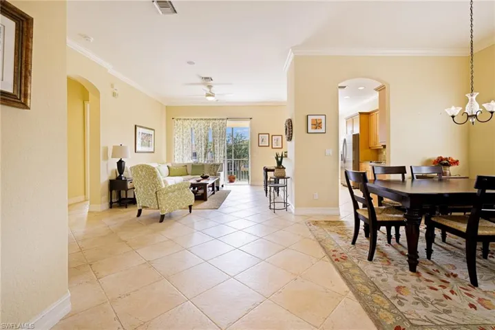 Dining room with ornamental molding, arched walkways, ceiling fan, light tile patterned flooring, and a chandelier