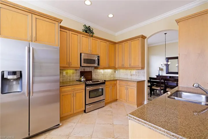 Kitchen with stainless steel appliances, a sink, light stone counters, backsplash, and ornamental molding