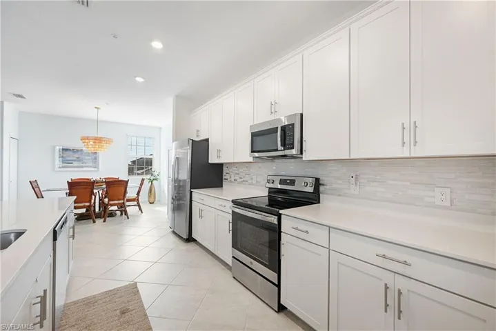 Kitchen with appliances with stainless steel finishes, white cabinets, hanging light fixtures, light tile patterned floors, and recessed lighting