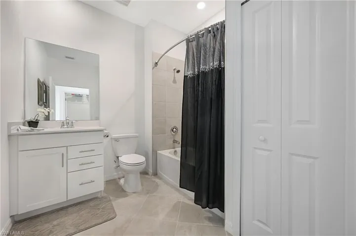 Bathroom featuring shower / bath combination with curtain, vanity, a closet, and light tile patterned floors
