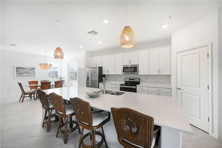 Kitchen featuring decorative light fixtures, white cabinets, appliances with stainless steel finishes, a breakfast bar area, and a spacious island