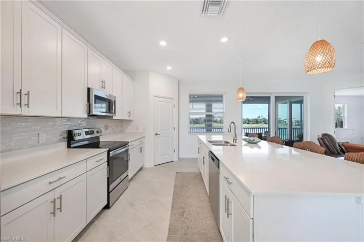 Kitchen with stainless steel appliances, hanging light fixtures, white cabinetry, a spacious island, and light stone counters