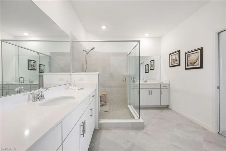 Full bathroom featuring a shower stall, two vanities, and light tile patterned flooring