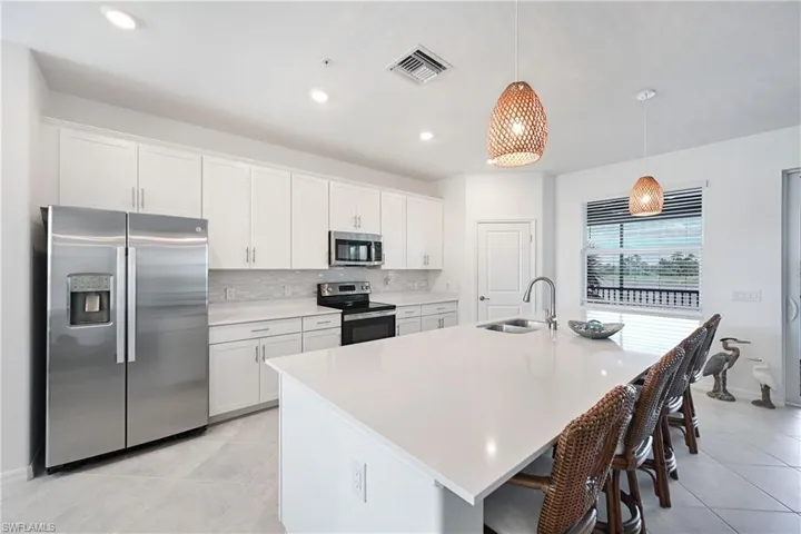 Kitchen featuring stainless steel appliances, white cabinetry, decorative light fixtures, a kitchen island with sink, and a kitchen breakfast bar