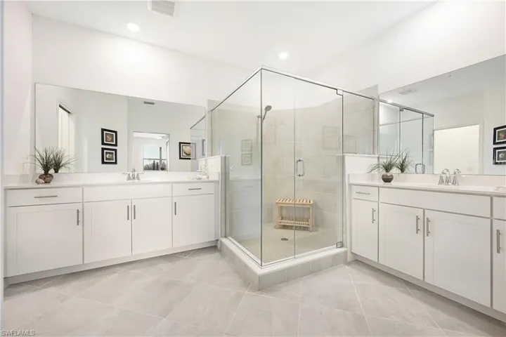 Bathroom featuring a stall shower, two vanities, light tile patterned floors, and recessed lighting