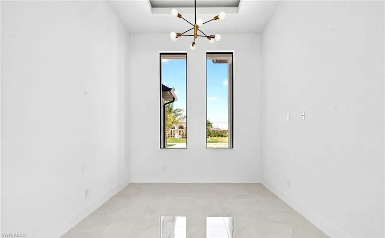This room features a modern chandelier, two tall windows, and light-colored tile flooring