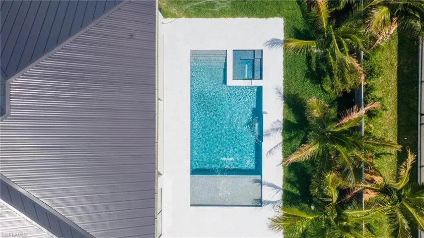 Aerial view showcasing a pristine swimming pool, surrounding patio area, and neatly maintained green lawn with palm trees