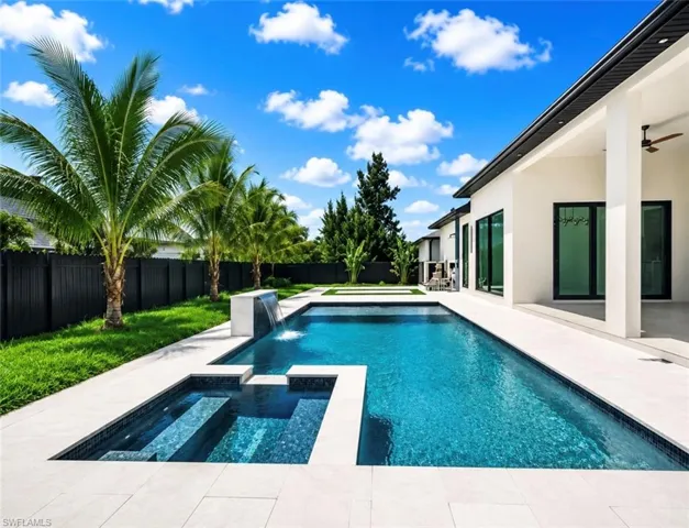 Expansive outdoor living area featuring a rectangular pool, integrated spa with waterfall feature, and light-toned patio pavers