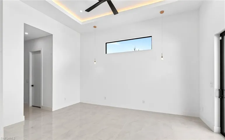 This living space features a tray ceiling with recessed lighting and a ceiling fan, sleek tile flooring, a horizontal window, and a door with a black frame