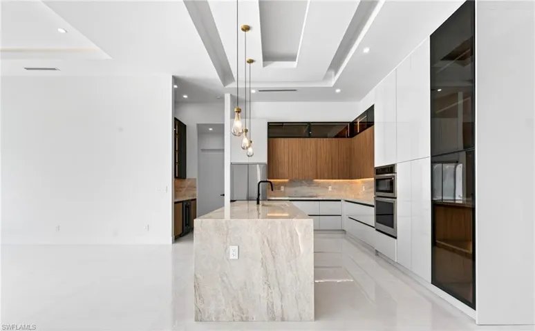 The modern kitchen features a waterfall island with a stone countertop, built-in stainless steel appliances, and a combination of white and wood-toned cabinetry